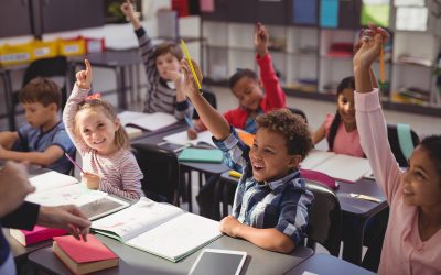 school children waving hands in classroom